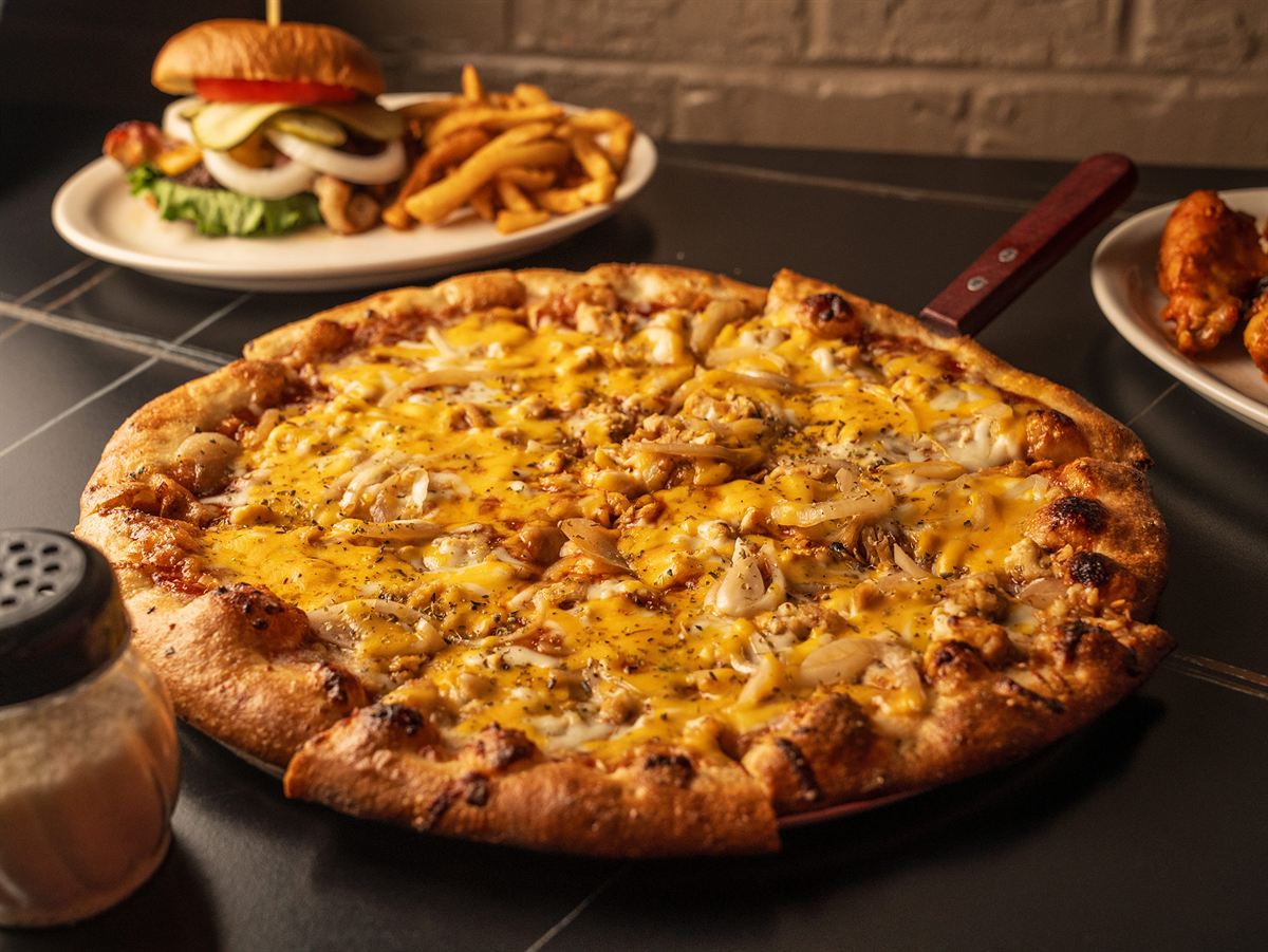 A cheese pizza with a burger and fries behind it