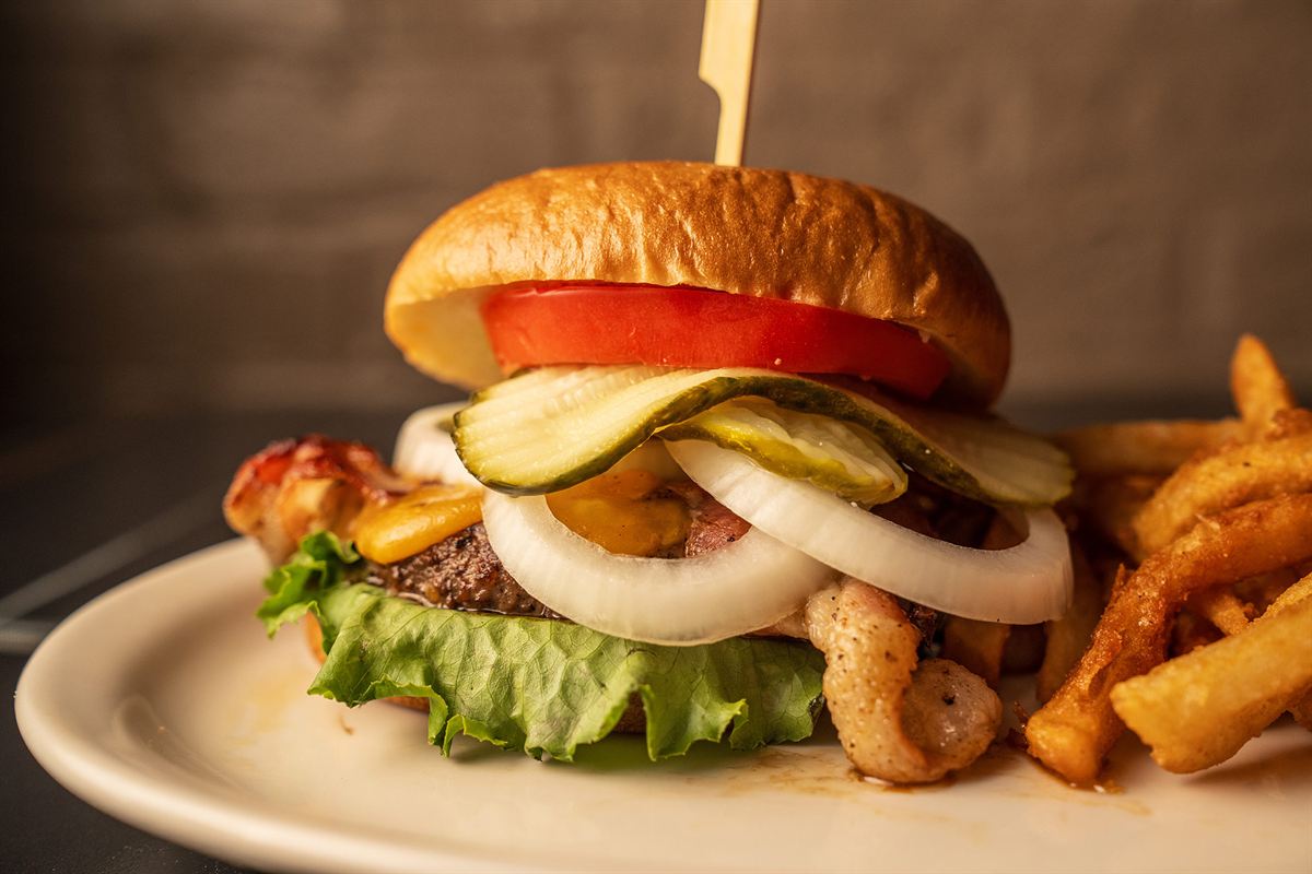 A burger with tomato, pickles, onion and fries
